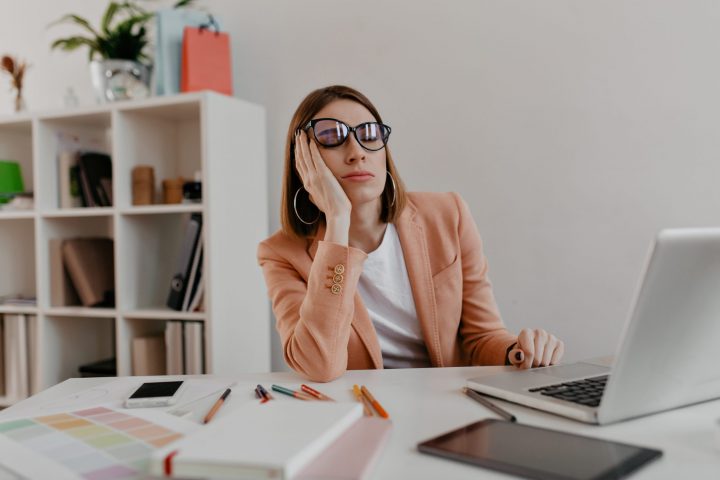 Tired worker wearing glasses falling asleep in workplace. Snapshot of lady in jacket in white office